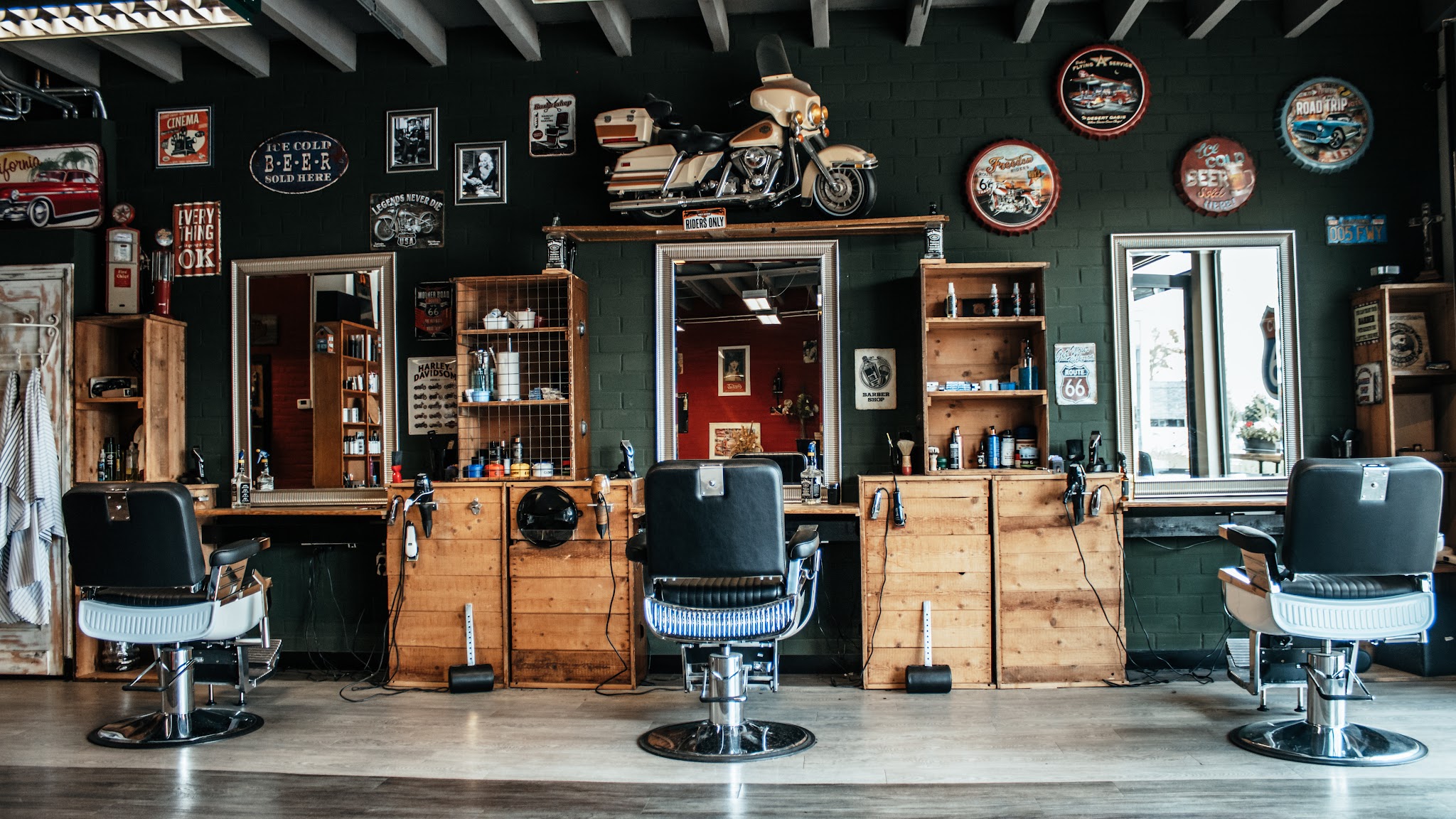 De salon van Coupe 66: houten werkplekken, drie zwarte barberstoelen en een motor aan de groene muur